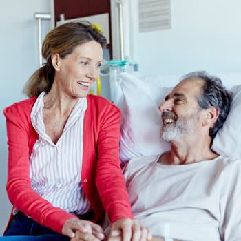 Wife smiles with husband while visiting him in hospital bed