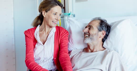 Wife smiles with husband while visiting him in hospital bed