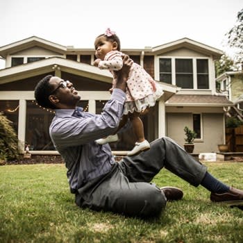 Father holds up his infant daughter while sitting on front lawn