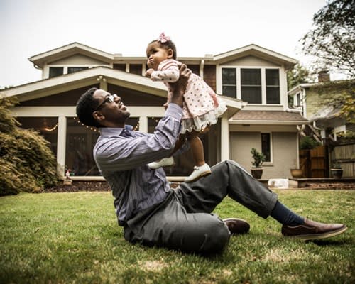 Father holds up his infant daughter while sitting on front lawn