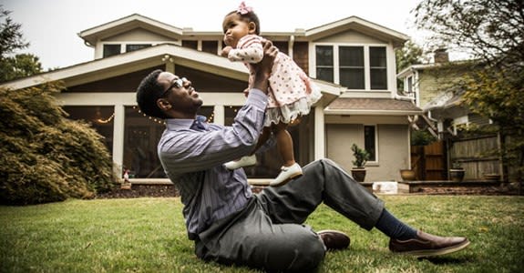 Father holds up his infant daughter while sitting on front lawn