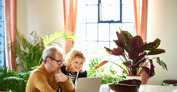 A smiling couple uses their laptop computer in a bright room at home