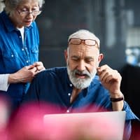 A man uses his home computer while his wife looks over his shoulder