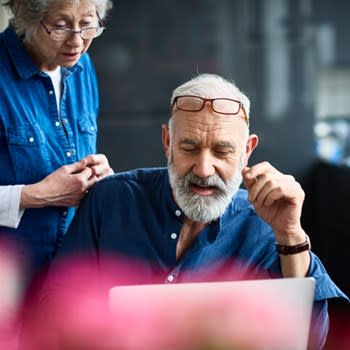 A man uses his home computer while his wife looks over his shoulder