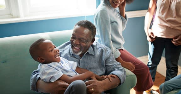 Smiling grandfather plays with young grandson on couch at home