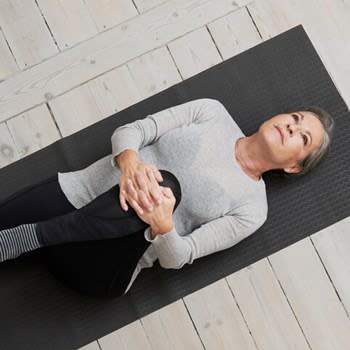 A woman lays on a yoga mat and stretches