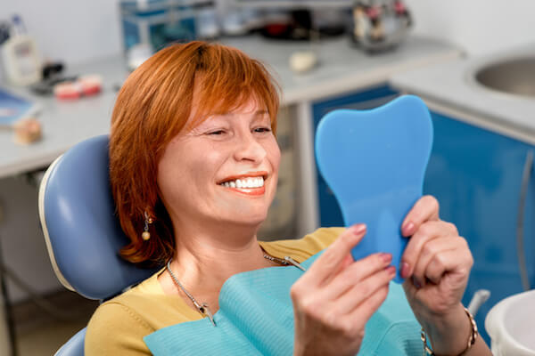 Woman smiles looking at her teeth in mirror in dentist chair