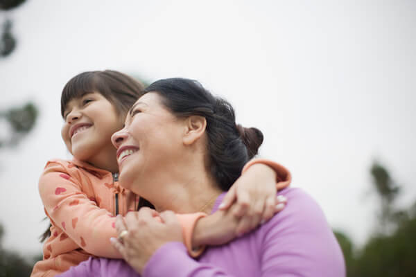 Woman and her granddaughter smiling outside with a blue sky background