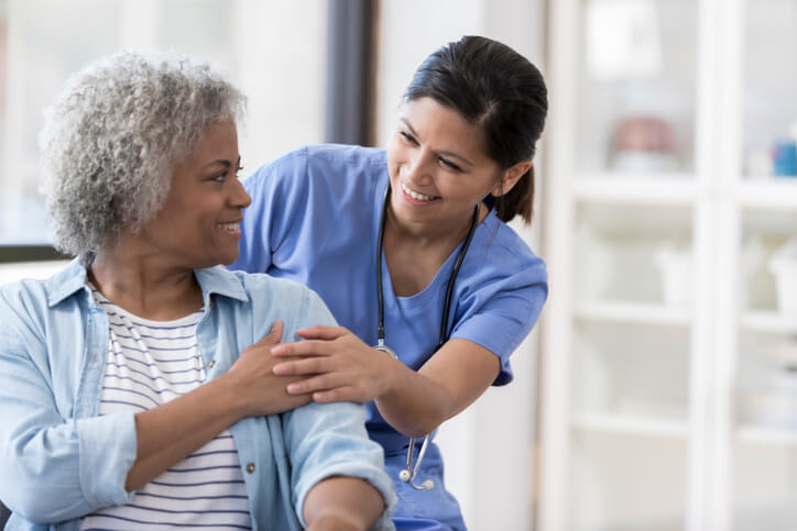 A woman and her nurse smile and hold hands