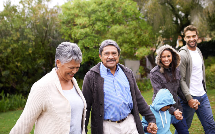 A family smiles while holding hands and walking outside