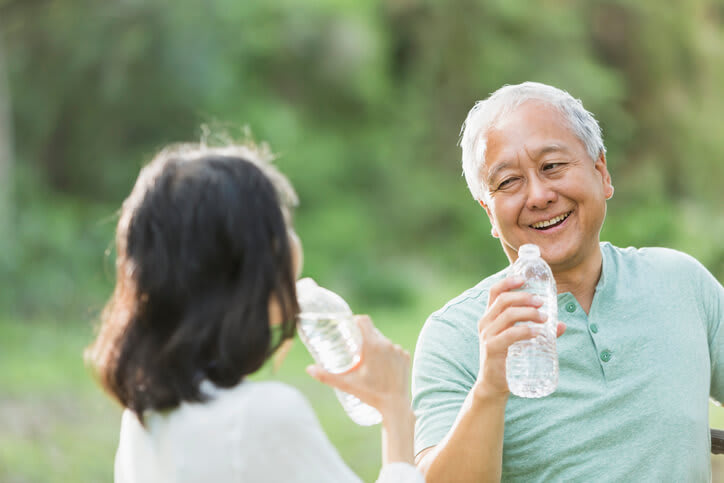 A smiling couple drinks from water bottles after exercise outside