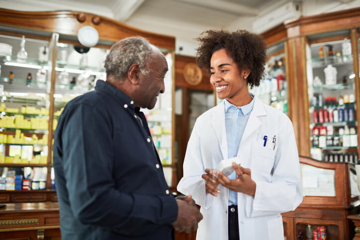 A pharmacist smiles and speaks to her patient about his medication