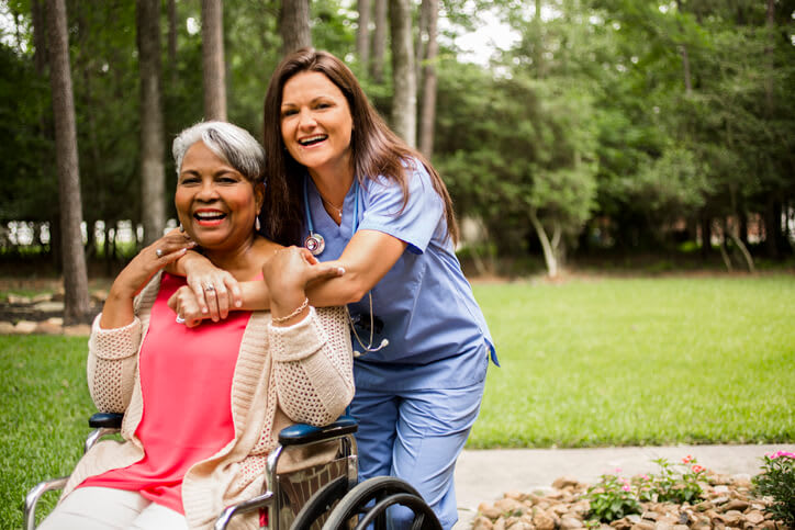 Nurse embraces patient in a wheelchair outside of nursing facility