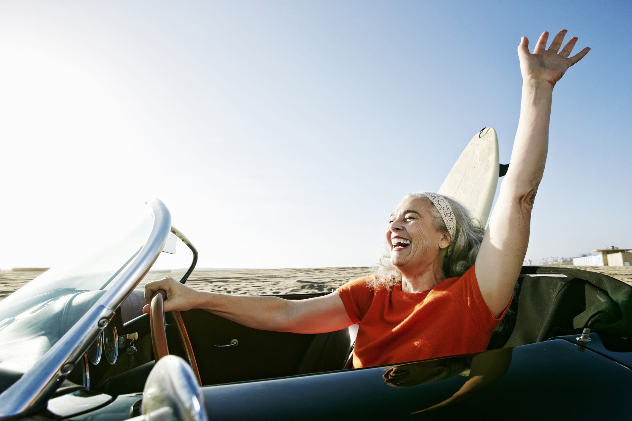 Woman In Convertible Car With Surfboard On Beach