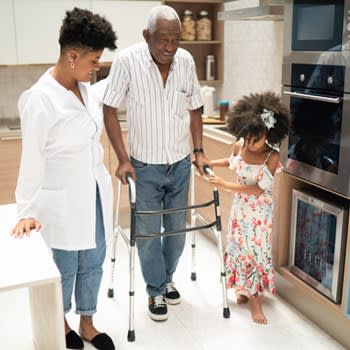Man assisted while using walker in his kitchen