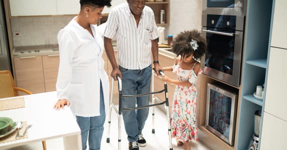 Man assisted while using walker in his kitchen