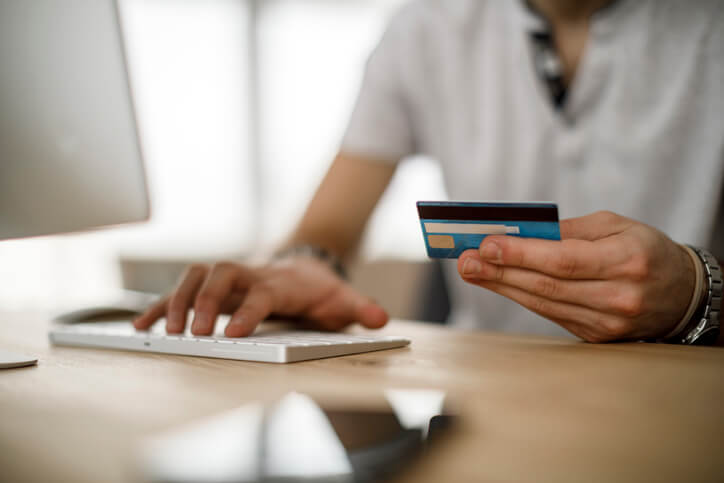 Someone holding credit card while typing on computer
