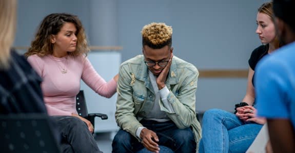 Young woman comforts fellow member of group therapy session