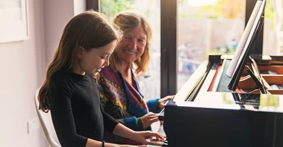 Smiling grandmother teaches granddaughter to play piano