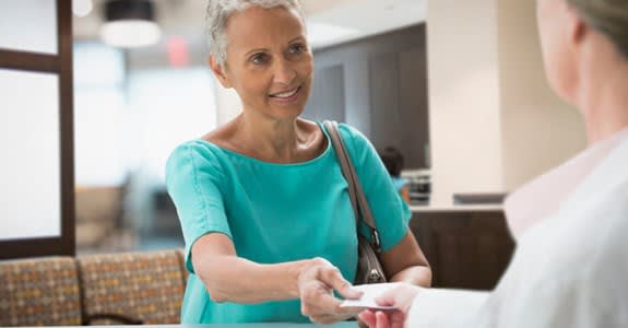 Woman hands her Medicare insurance card to office worker at doctor's office