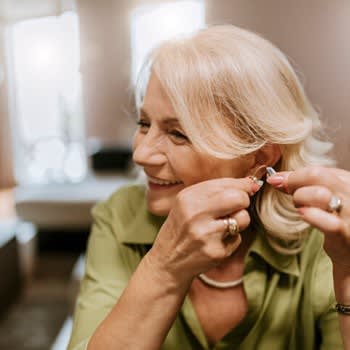 Woman smiles and fits on her hearing aids