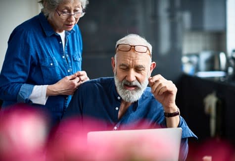 A man uses his home computer while his wife looks over his shoulder
