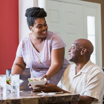 Family caregiver serves lunch to her father