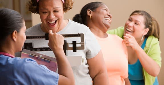 A group of women laugh and celebrate while weighing in for a weight loss group
