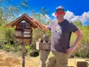 Jon Beardmore standing outside next to the Galapagos postbox made out of an old wooden barrel affixed to a post.