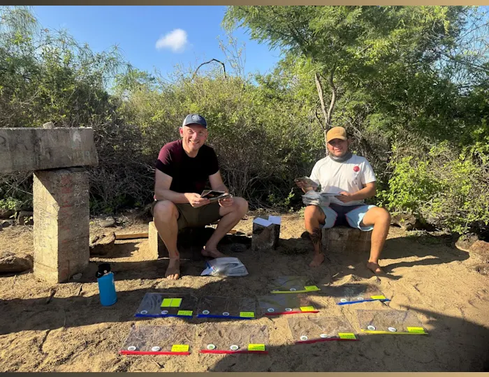Jon Beardmore sitting outside with another person sorting through postcards