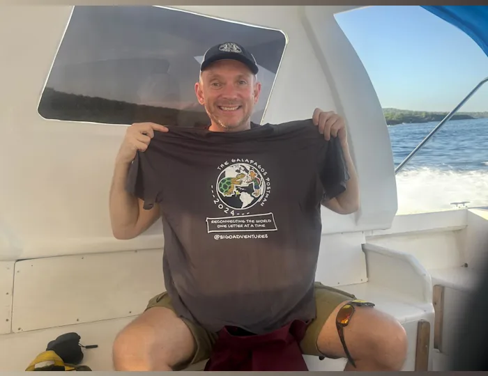 Jon Beardmore holding a t-shirt with the text "The Galapagos Postman 2024"