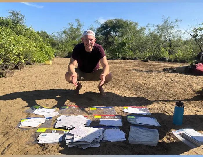 Jon Beardmore crouching down in front of a large collection of postcards on the ground that have been sorted.