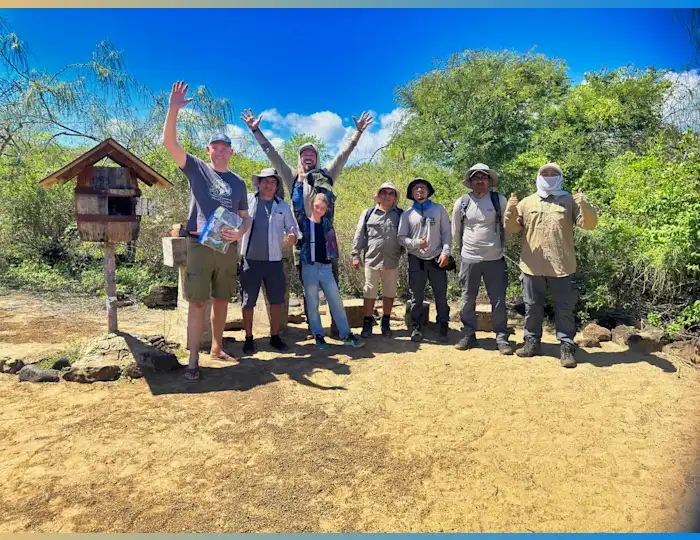 A group of eight people standing next to the Galapagos postbox with their arms raised in the air.