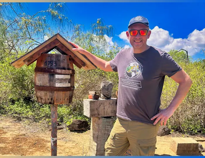 Jon Beardmore standing outside next to the Galapagos postbox made out of an old wooden barrel affixed to a post.