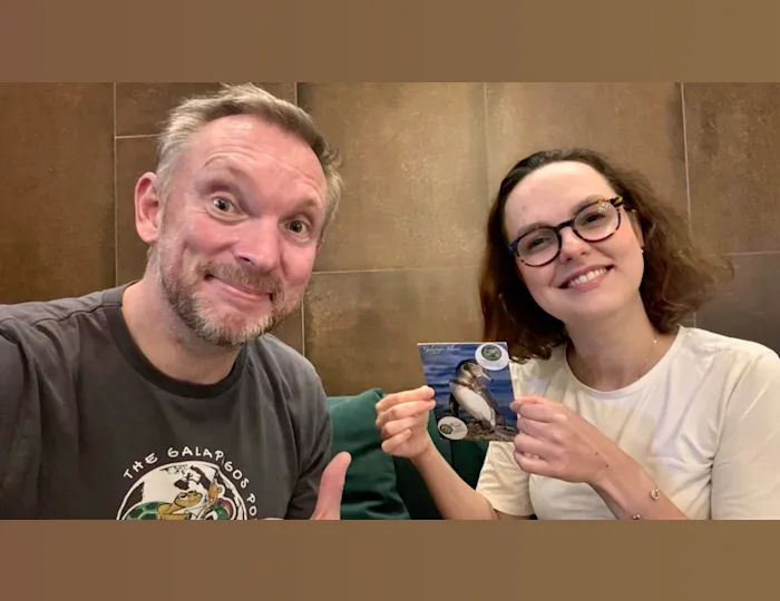 Jon Beardmore handing a postcard with a picture of a penguin on it to a woman who is smiling.