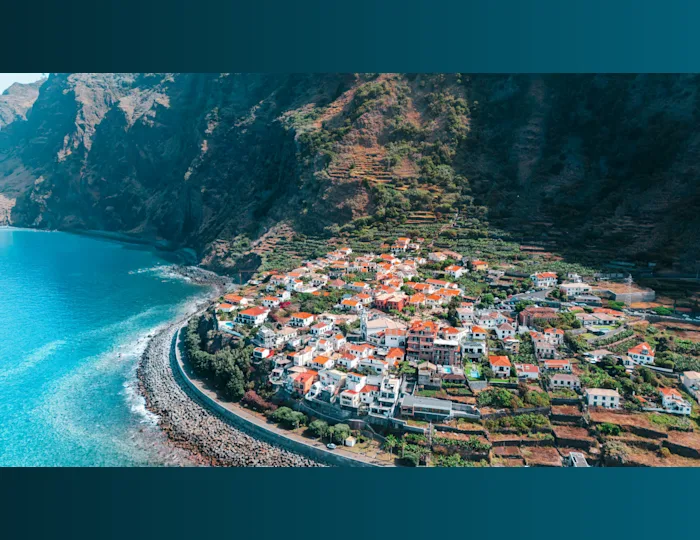 Stunning aerial view of a coastal town in Madeira, Portugal, with lush cliffs and turquoise sea. Photo credit: Ryan Klaus (ryanklaus.ch)