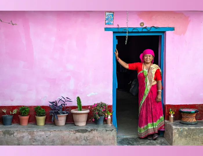 The Aathpahariya community at Khambela, Dhankuta, greets guests on arrival. A woman in a traditional red sari stands in the doorway of a pink house.