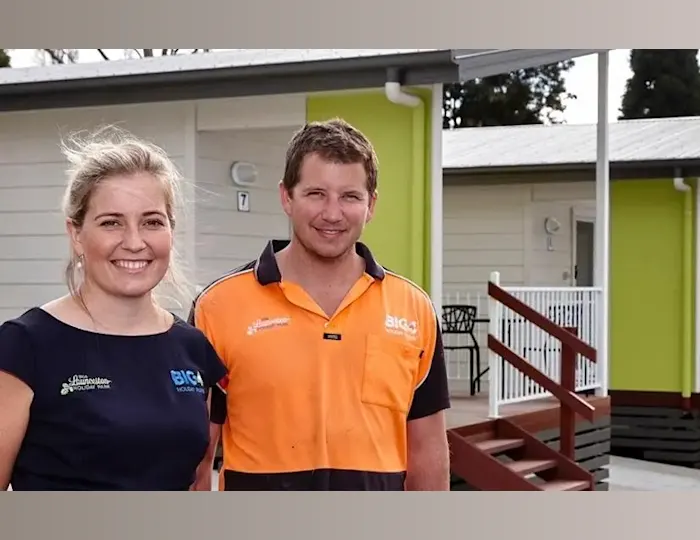 A smiling woman and man in BIG4 work shirts standing in front of a cabin with a lime-green wall at a holiday park in Launceston.