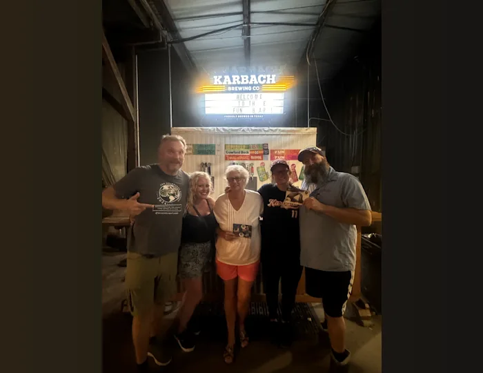 Jon Beardmore in an outdoor bar with four people. Two people are holding a postcard he has delivered to them.