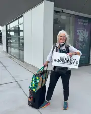 A friendly woman holding an "ability adventures" sign