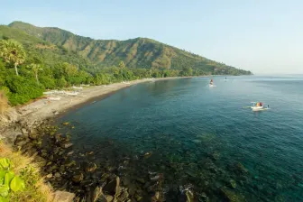A picture of a bay with blue water and a beach, with tropical jungle on the hills behind