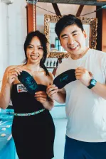 An young woman in a black dress and young man wearing a white t-shirt posing while holding Nappr branded sleeping masks and smiling
