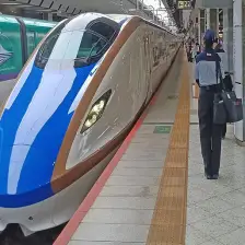 The front of a bullet train at a train station in Japan. The train has a blue nose and white sides.