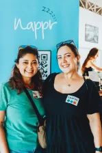 Two women posing for a photo in front of a blue rollup banner with the brand Nappr on a blue background