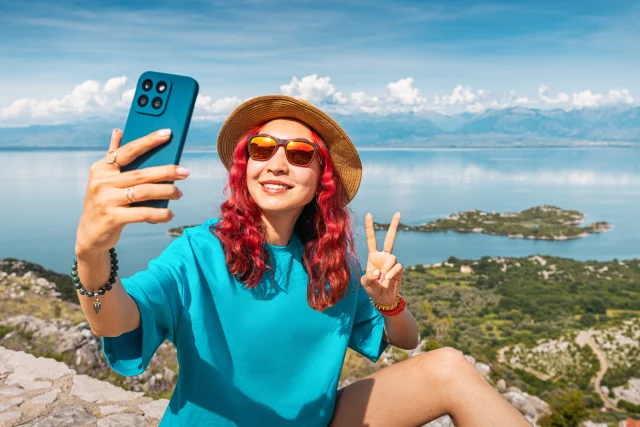 Picture of a women taking a selfie on top of a mountain with a view of the sea and coastline behind her.