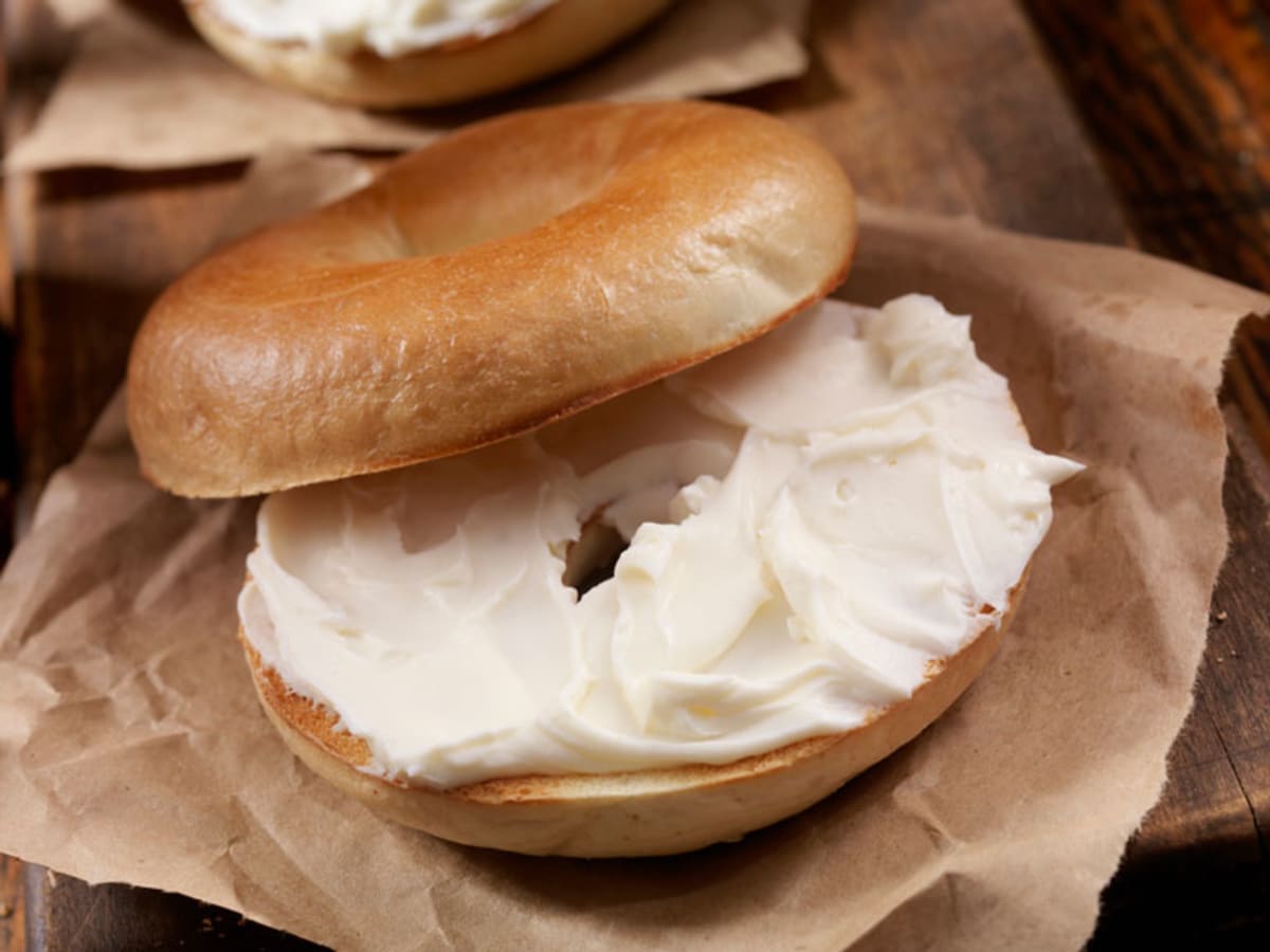 White bagel with cream cheese on cardboard wrapping.