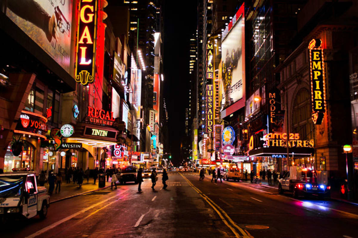 People walking along bright Theater District street at night.