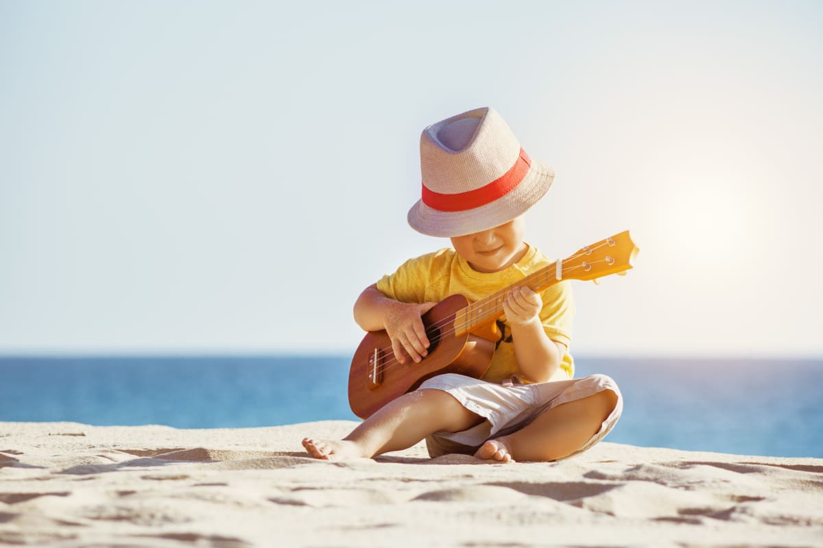 Young toddler playing ukulele on beach