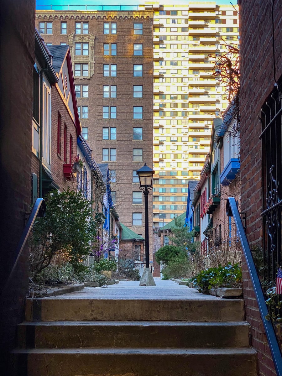 Pomander Walk in NYC - a small private through-street with British Tudor style homes on either side of the street and traditional lamps - NYC sky scrapers in the background. 