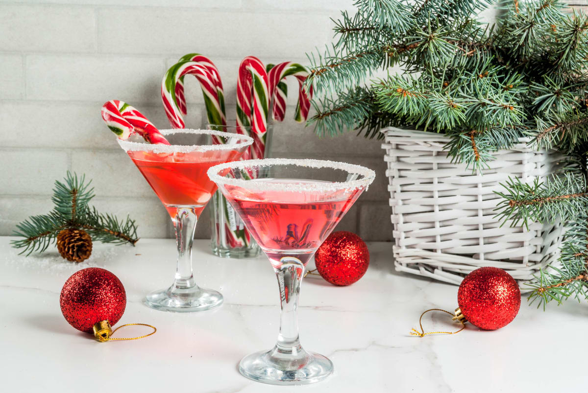 Two red Christmas cocktails in martini glasses with candy canes and christmas decor in the background. 